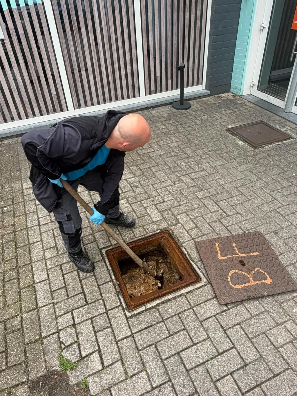 Technicien Nero Canalis nettoyant un regard d’égout devant un commerce à Ronse, intervention service area étendu